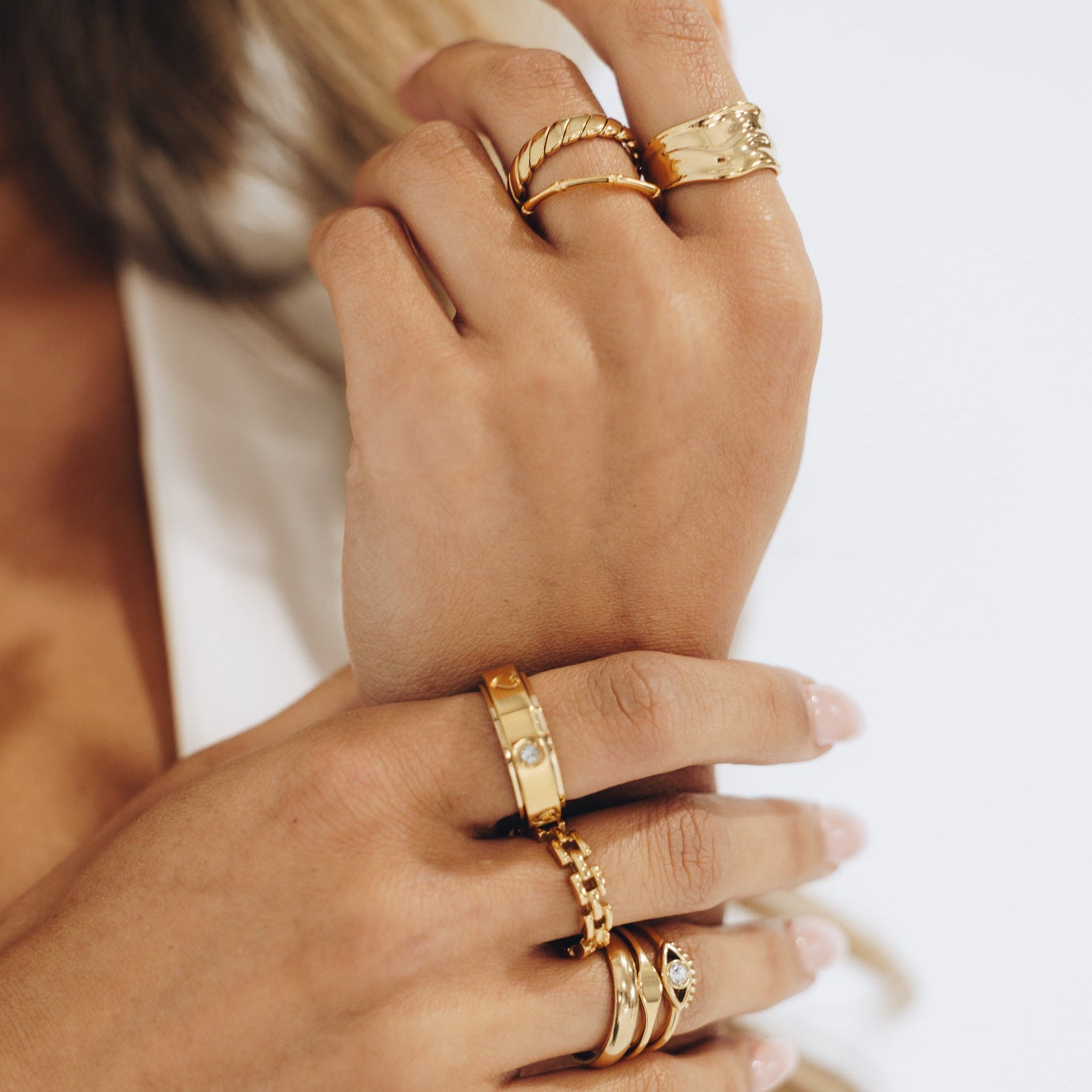 Close-up of hands wearing multiple gold rings on a neutral background