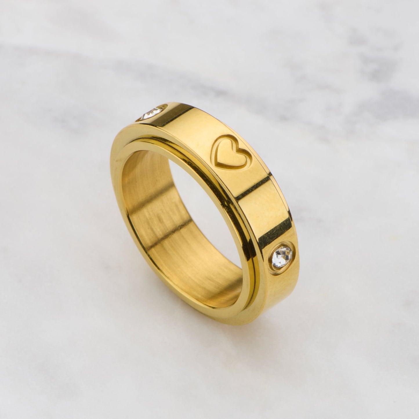Gold ring with heart and diamond design on a marble background