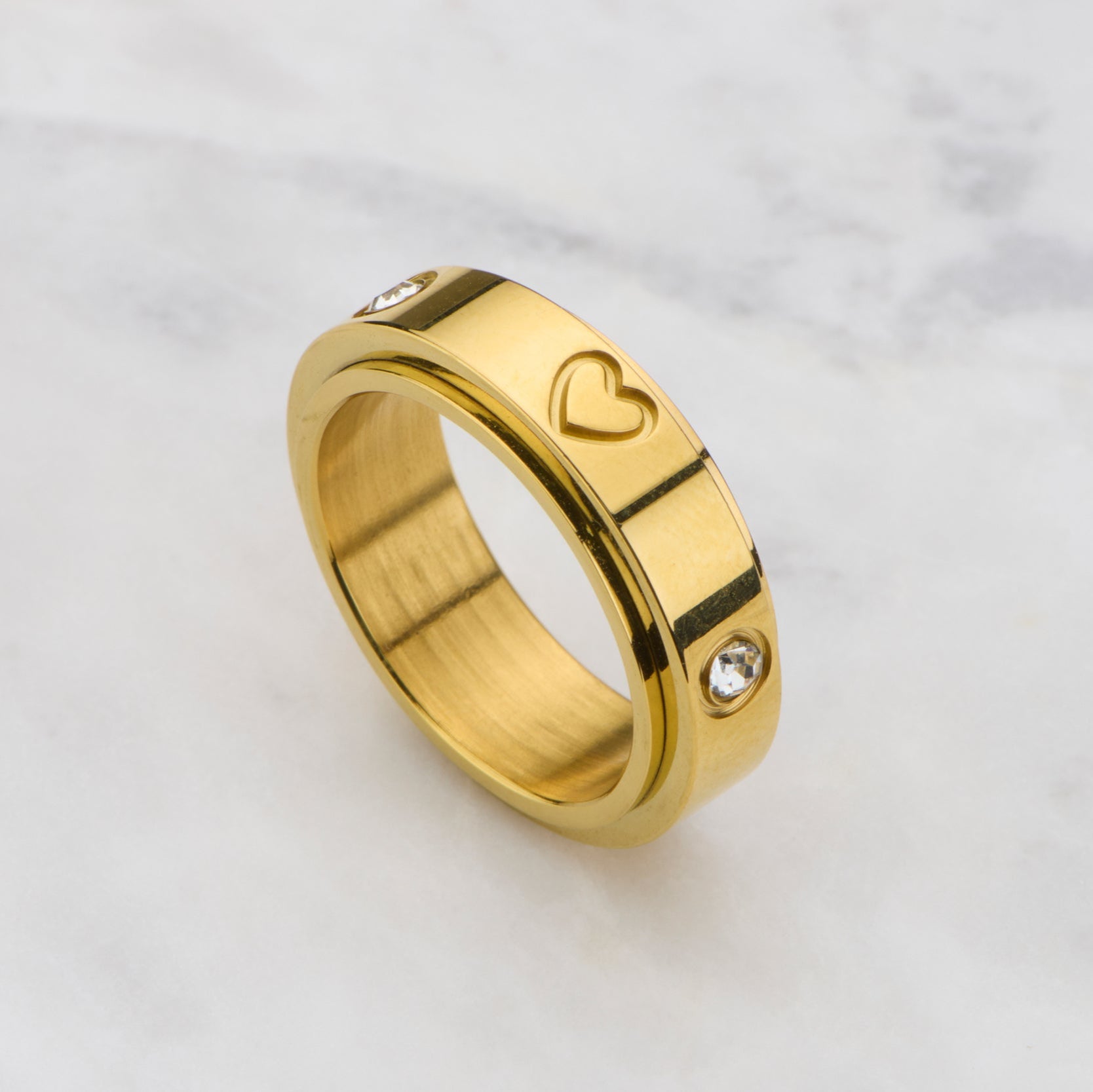 Gold ring with heart and diamond design on a marble background