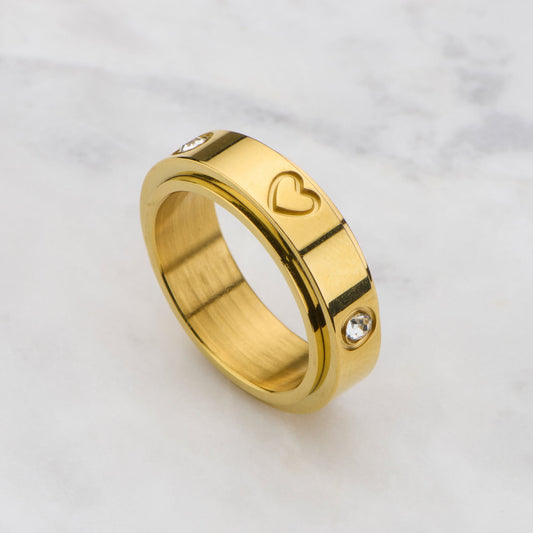 Gold ring with heart and diamond design on a marble background
