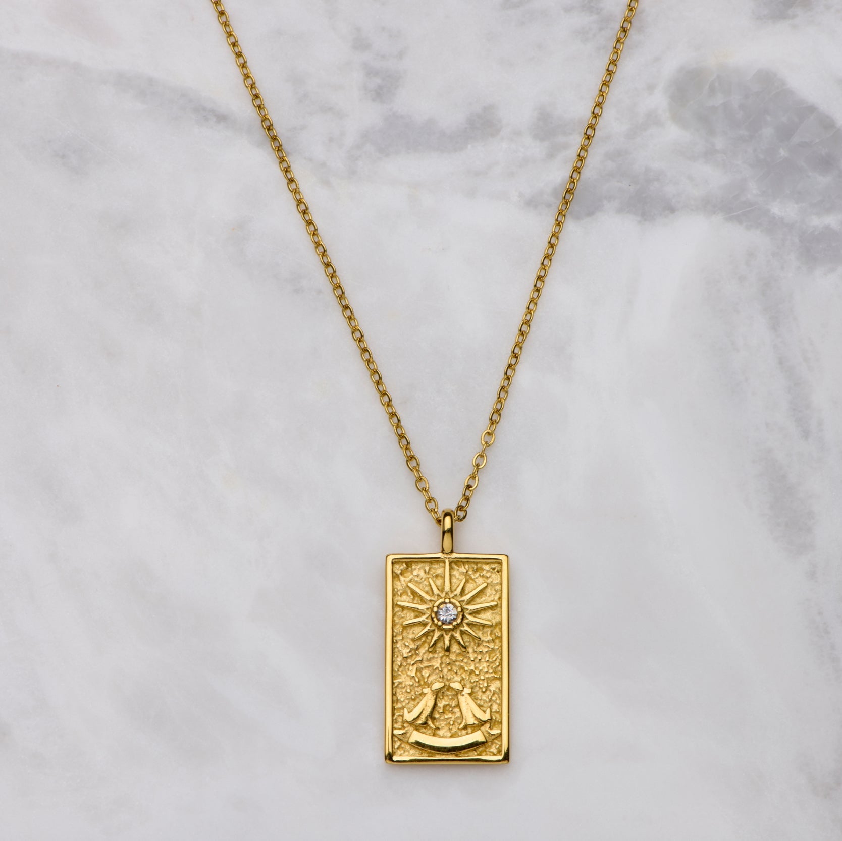 Gold necklace with a rectangular pendant on a marble background