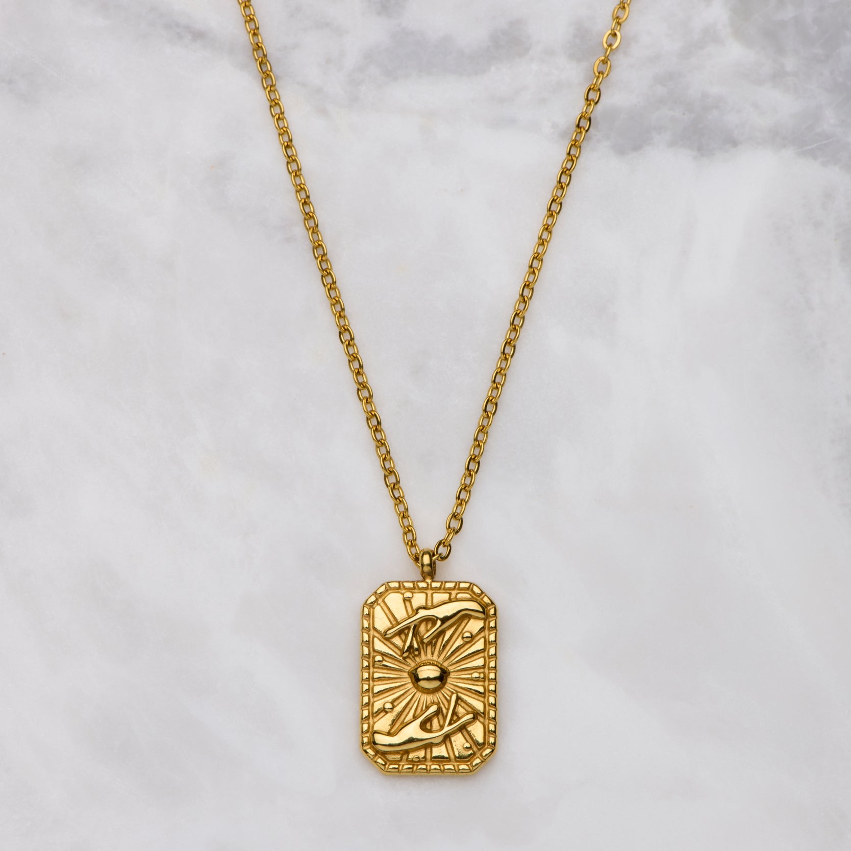 Gold necklace with a rectangular pendant on a marble surface