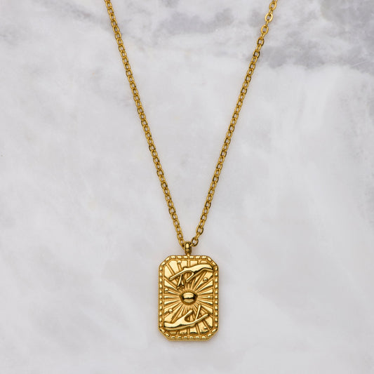 Gold necklace with a rectangular pendant on a marble surface