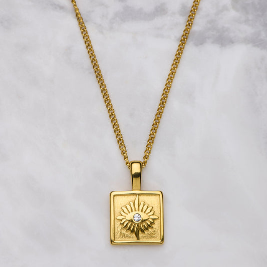 Gold necklace with a square pendant on a marble background