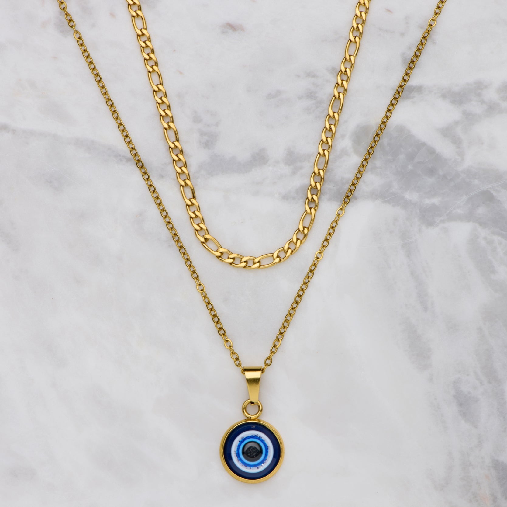 Gold necklace with a blue evil eye pendant on a marble background