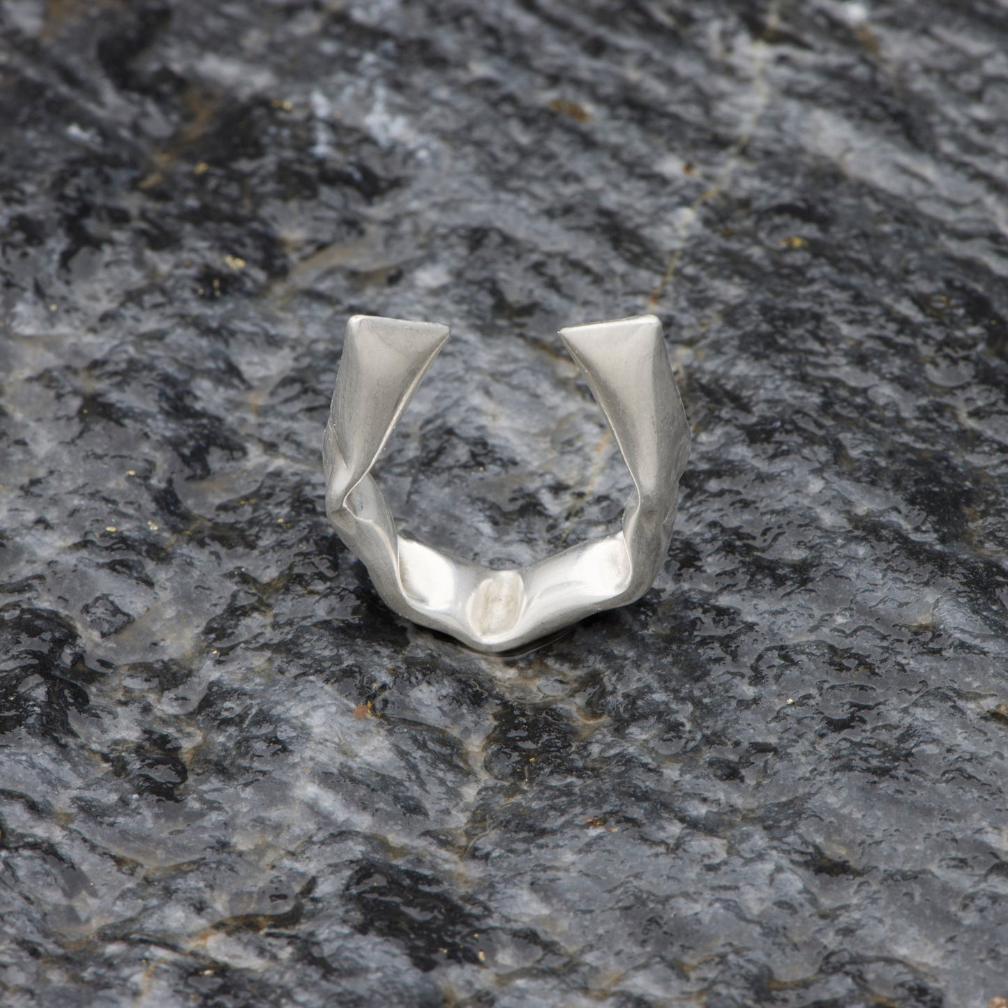 Silver ring with geometric design on a dark stone surface