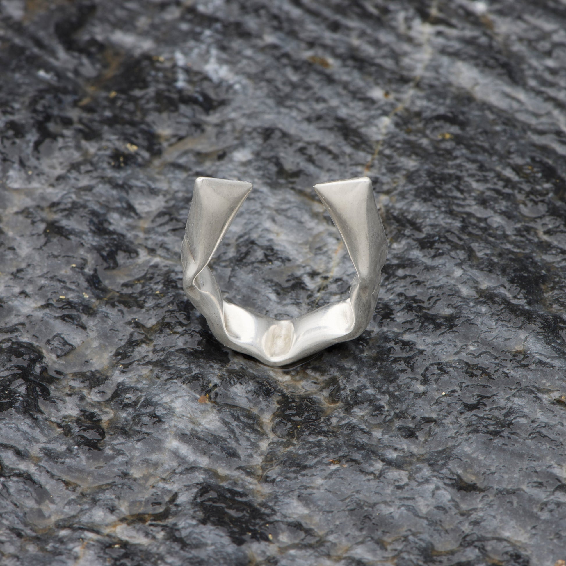 Silver ring with geometric design on a dark stone surface