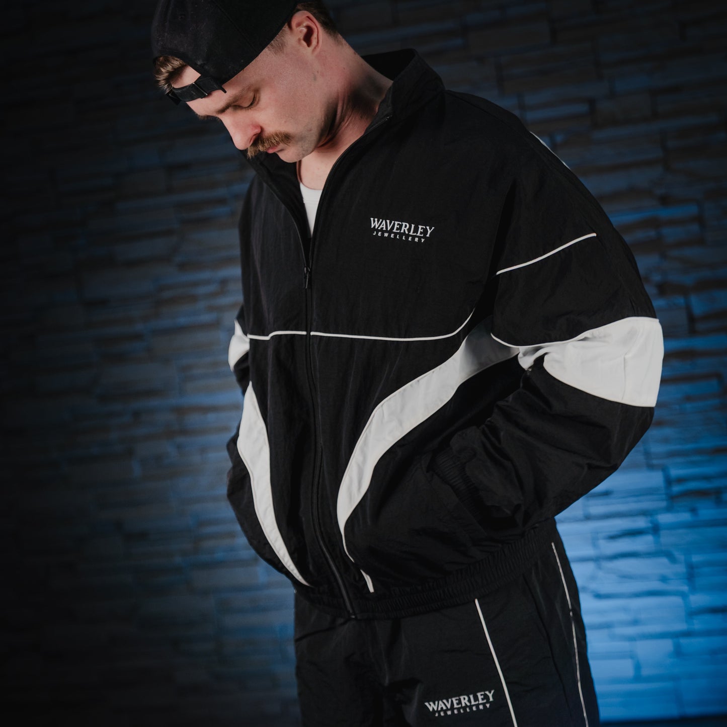 Person wearing a black and white tracksuit with 'Waverley' branding against a dark brick wall.