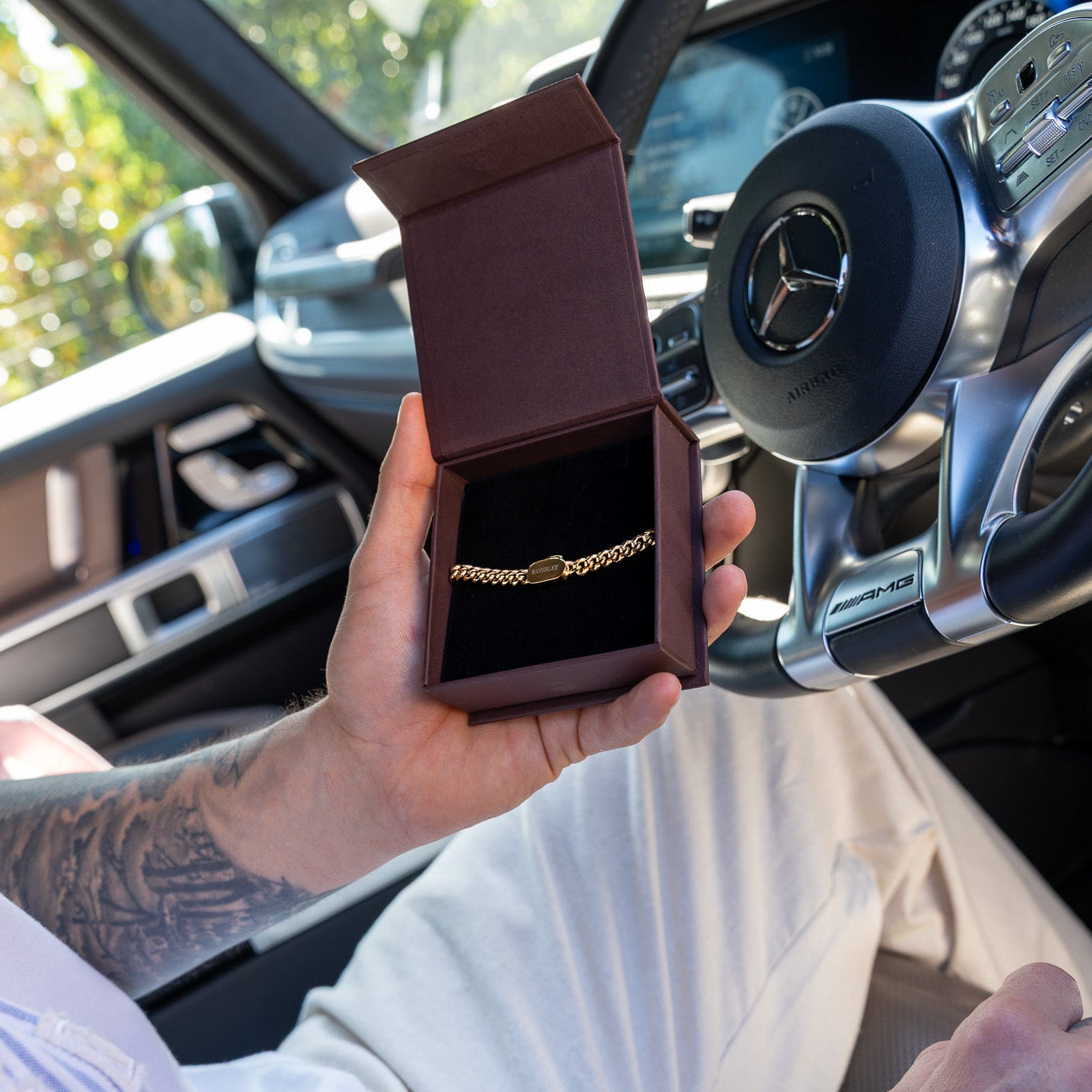 Person holding a jewelry box with a gold necklace inside, sitting in a car.