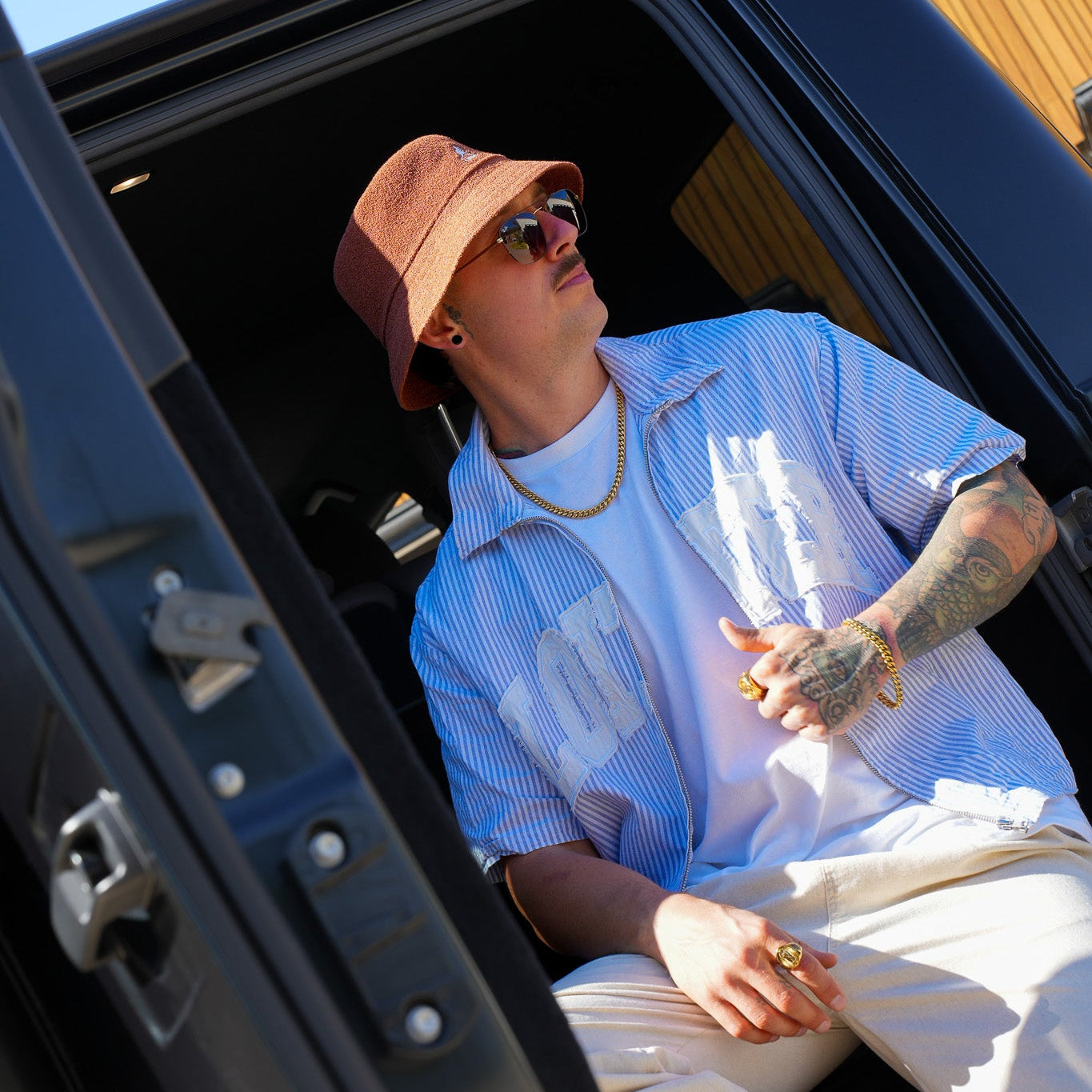 Person sitting in an open car door wearing a blue shirt and beige pants.