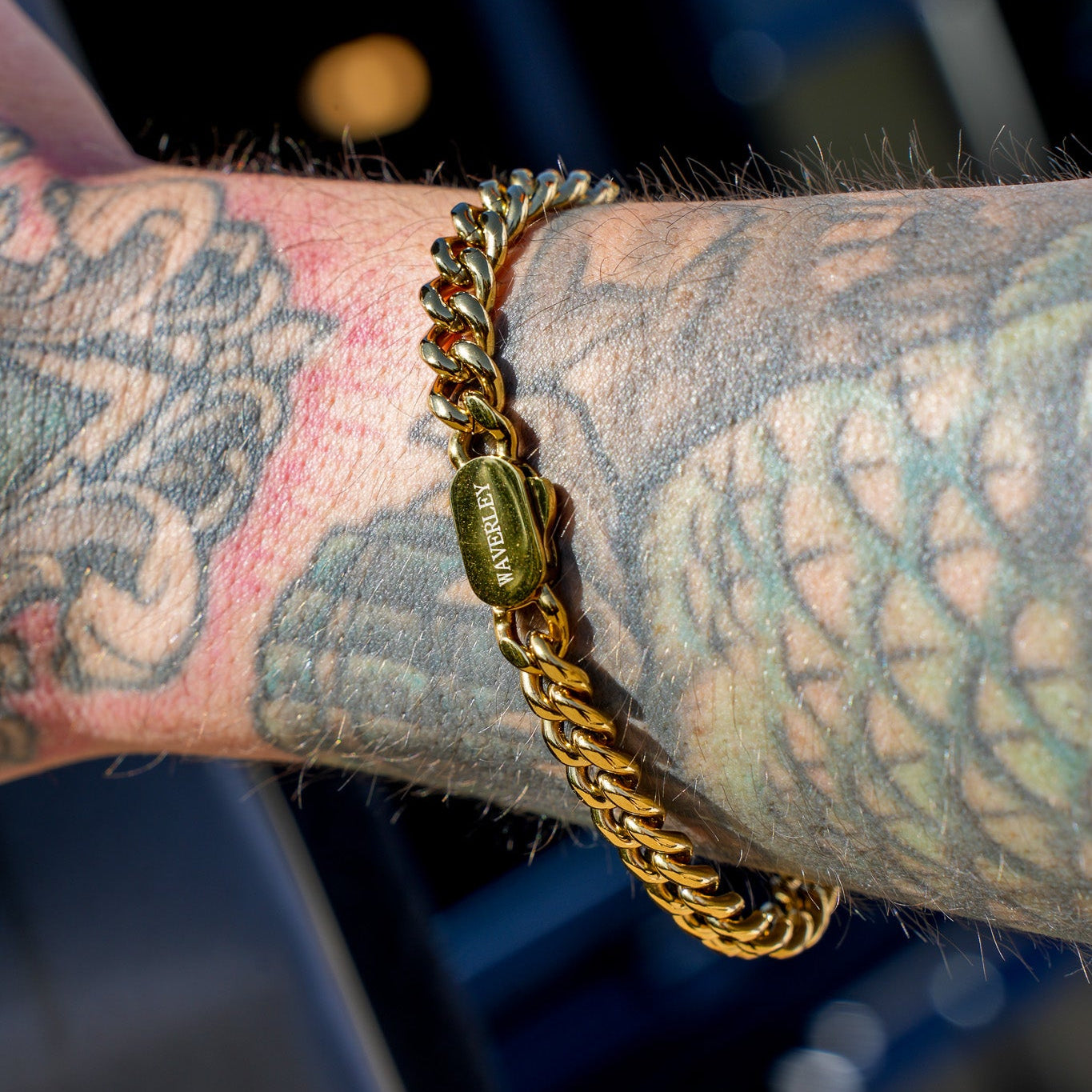 Gold chain bracelet on a tattooed arm with a blurred background