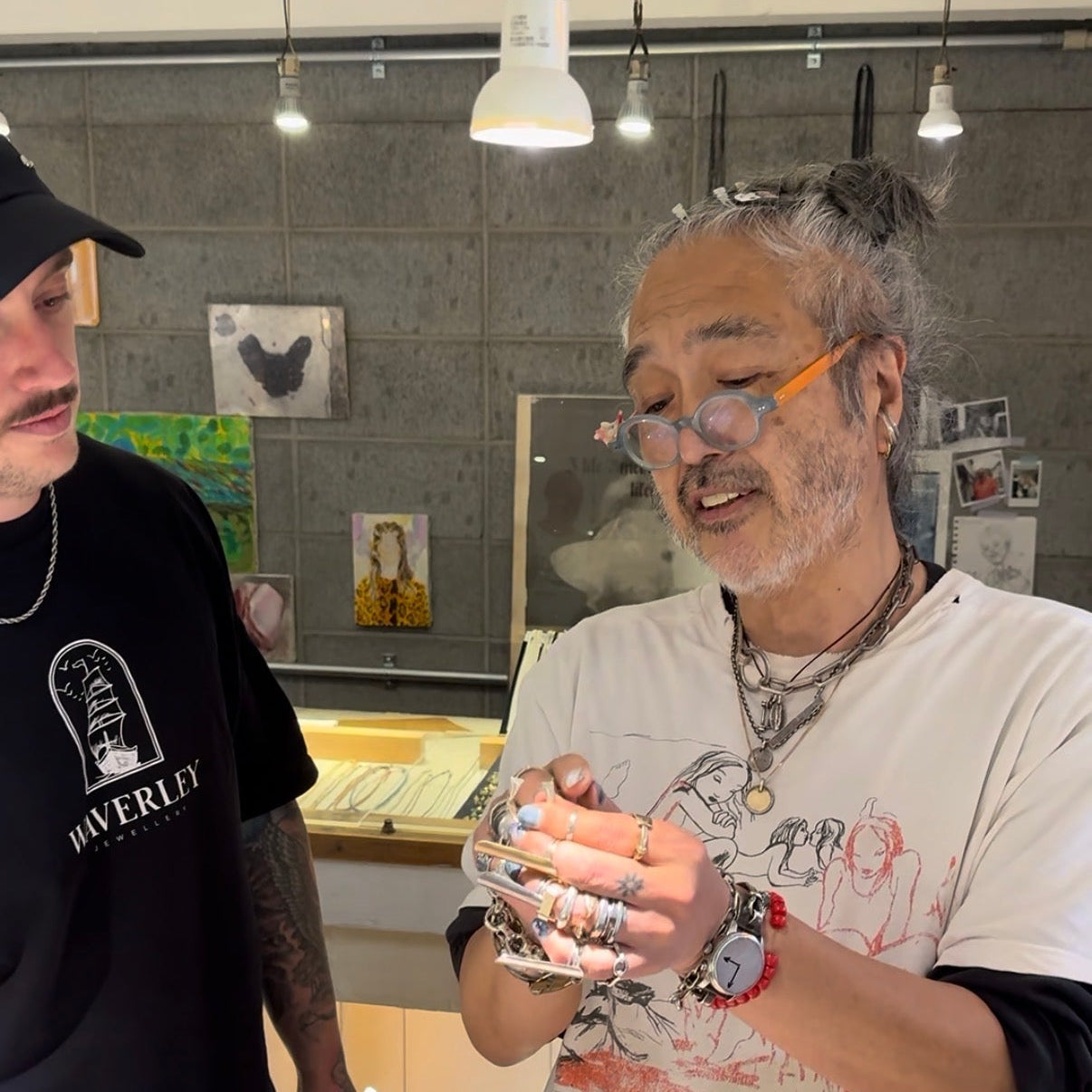 Two men in a workshop setting, one holding metal components.