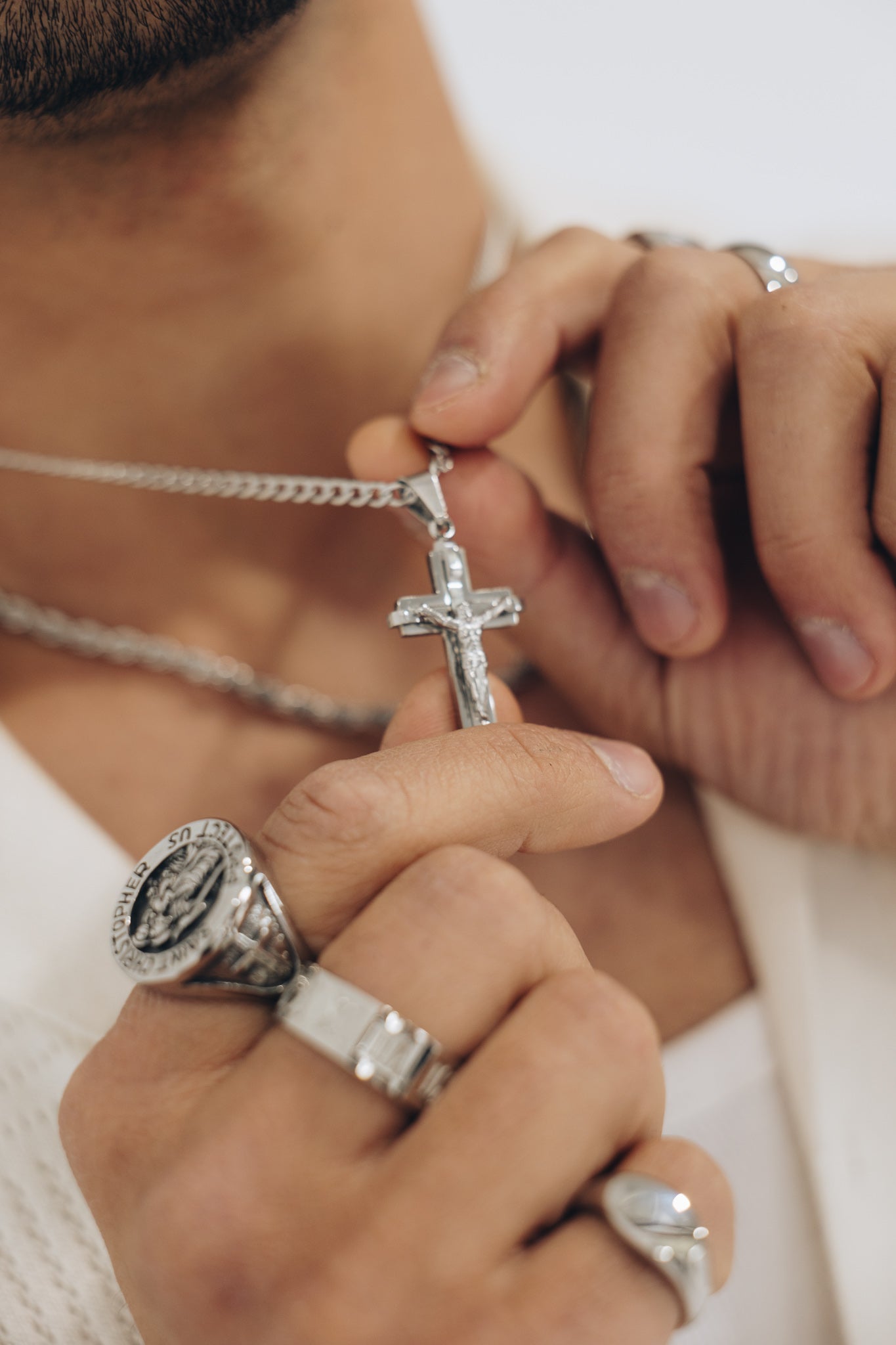 Close-up of hands wearing silver rings and a necklace with a cross pendant.