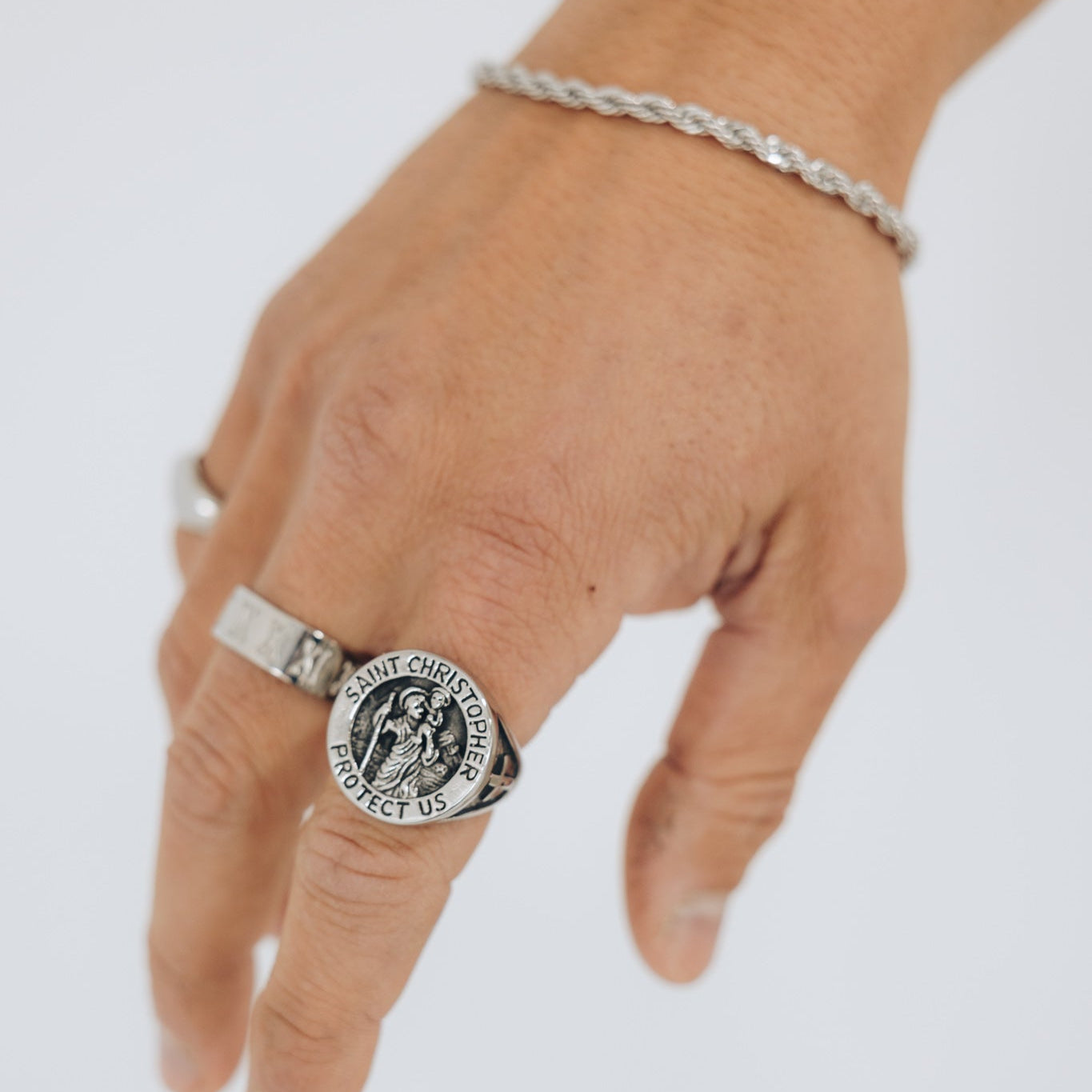 Hand wearing a silver ring with a detailed design on a white background