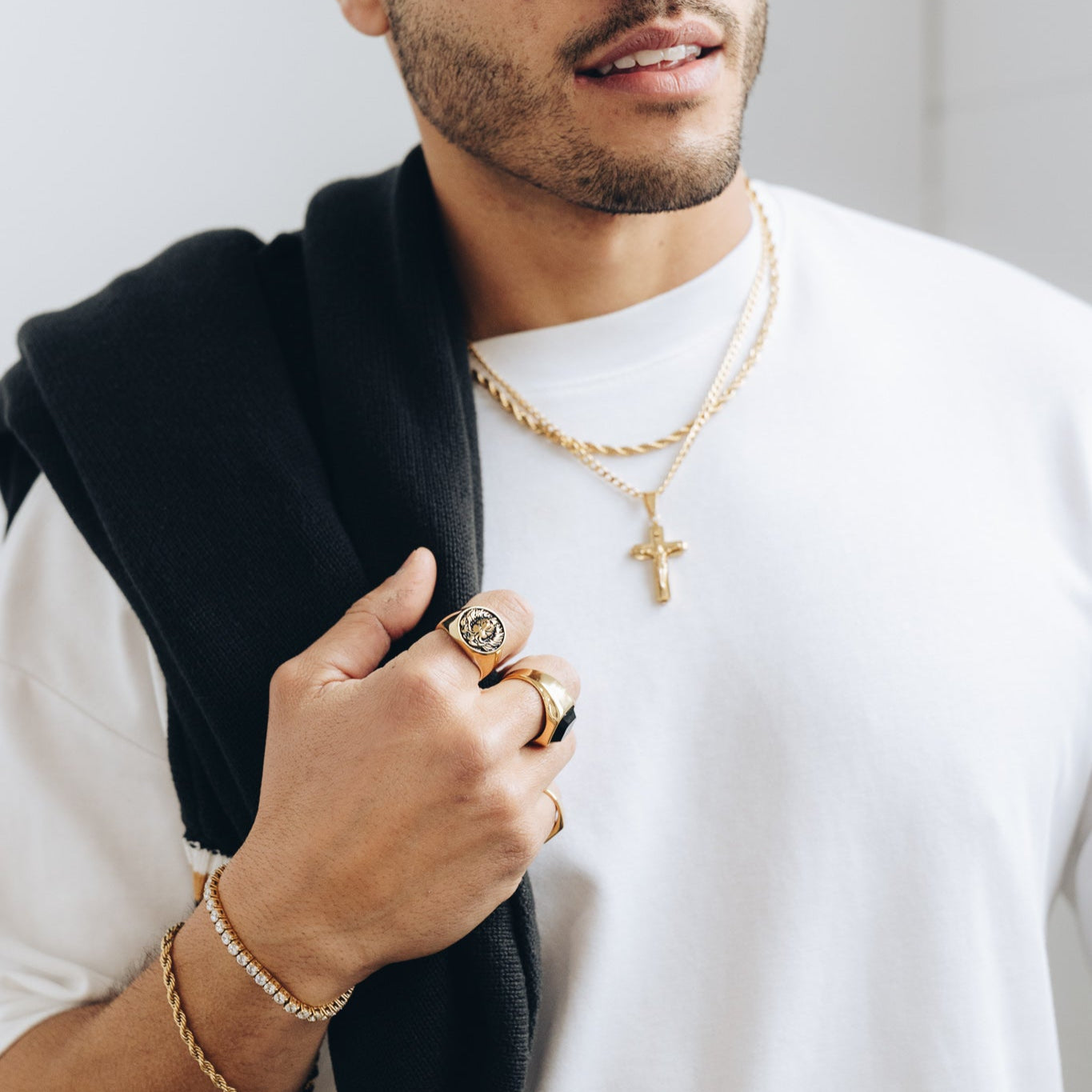 Man wearing a white shirt, black cap, and gold jewelry against a plain background and gold chain